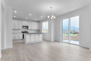 Kitchen with white cabinetry, an island with sink, tasteful backsplash, appliances with stainless steel finishes, and decorative light fixtures