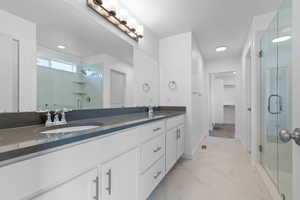 Bathroom featuring a stall shower, double vanity, light marble finish floors, a spacious closet, and recessed lighting