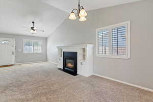 Unfurnished living room with carpet, high vaulted ceiling, a fireplace with flush hearth, a ceiling fan, and a chandelier