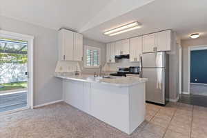 Kitchen with appliances with stainless steel finishes, light countertops, white cabinets, and a peninsula