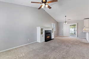 Unfurnished living room with light colored carpet, high vaulted ceiling, a fireplace with flush hearth, and a ceiling fan