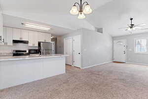 Kitchen with white cabinets, lofted ceiling, light colored carpet, stainless steel appliances, and a peninsula