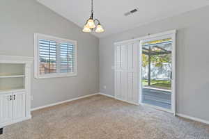 Spare room with lofted ceiling, light colored carpet, a chandelier, and built in features