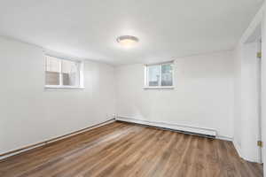 Below grade area featuring wood finished floors, a baseboard radiator, and healthy amount of natural light