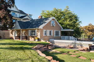 Rear view of house featuring brick siding, a chimney, a shingled roof, a deck, and a patio area