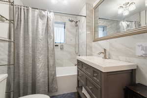 Full bathroom featuring shower / bath combo with shower curtain, tile walls, and vanity