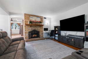 Living area with dark wood finished floors, a fireplace, a ceiling fan, and a desk