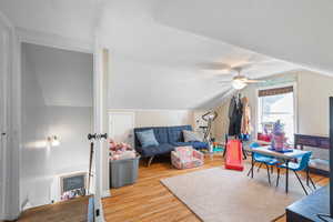 Rec room featuring wood finished floors, a textured ceiling, vaulted ceiling, and a ceiling fan