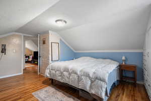 Bedroom featuring a textured ceiling, vaulted ceiling, and wood finished floors