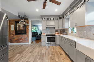 Kitchen with gray cabinets, appliances with stainless steel finishes, glass insert cabinets, ceiling fan, and healthy amount of natural light