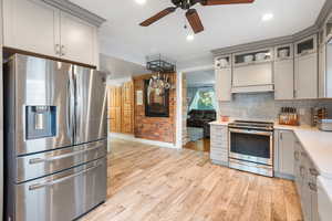 Kitchen featuring stainless steel appliances, gray cabinetry, ceiling fan, decorative backsplash, and light wood-type flooring