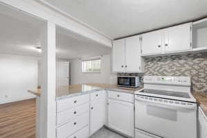 Kitchen featuring a textured ceiling, white appliances, white cabinets, a peninsula, and tasteful backsplash
