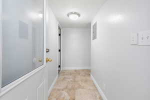 Corridor featuring electric panel and light stone finish floors