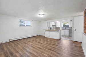 Unfurnished living room featuring dark wood-style floors, baseboard heating, and a textured ceiling