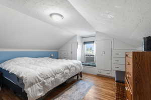 Bedroom featuring a textured ceiling, wood finished floors, vaulted ceiling, and cooling unit