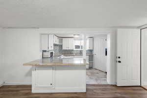 Kitchen with a peninsula, white cabinets, a textured ceiling, dark wood-style flooring, and light stone countertops