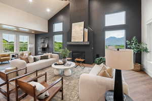 Living room with wood finished floors, high vaulted ceiling, a glass covered fireplace, plenty of natural light, and recessed lighting