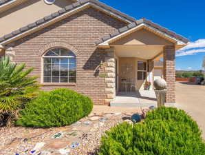 Property entrance with brick siding, a porch, stucco siding, stone siding, and a garage