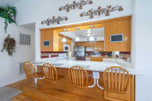 Kitchen with decorative backsplash, stainless steel appliances, light wood-style flooring, a kitchen breakfast bar, and pendant lighting