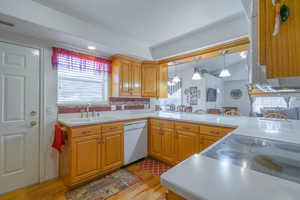Kitchen with hanging light fixtures, light wood finished floors, light countertops, white dishwasher, and tasteful backsplash
