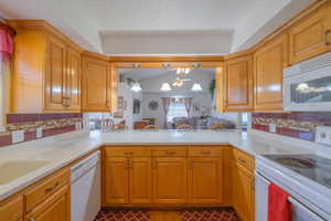 Kitchen featuring decorative backsplash, white appliances, pendant lighting, and brown cabinetry