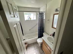 Full bath featuring shower / bath combo with shower curtain, vanity, light tile patterned flooring, and a textured ceiling