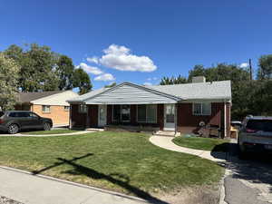 View of front of house with a front yard, brick siding, a chimney, and a shingled roof