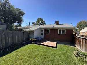 Rear view of house with a deck, brick siding, a fenced backyard, and a shingled roof