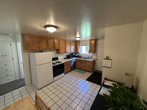 Kitchen featuring light countertops, freestanding refrigerator, brown cabinetry, gas range oven, and light tile patterned flooring