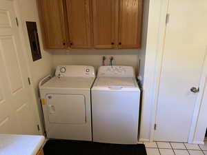 Laundry room featuring light tile patterned floors, electric panel, cabinet space, and independent washer and dryer