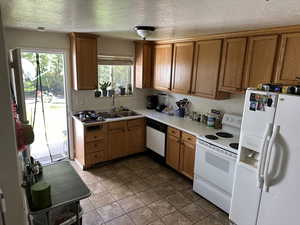 Kitchen featuring white appliances, a textured ceiling, light countertops, dark tile patterned flooring, and brown cabinets