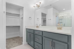 Full bathroom with a spacious closet, double vanity, a stall shower, and light carpet