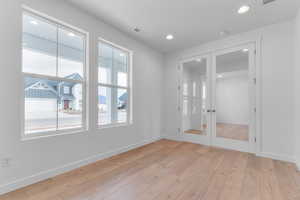 Empty room with light wood-style flooring, recessed lighting, french doors, and a residential view