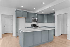 Kitchen with gray cabinets, appliances with stainless steel finishes, light wood-style flooring, and recessed lighting