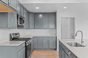 Kitchen featuring appliances with stainless steel finishes, light wood-type flooring, gray cabinets, recessed lighting, and light stone counters