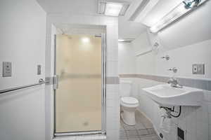 Full bath featuring tile walls, a shower stall, light tile patterned flooring, and a wainscoted wall