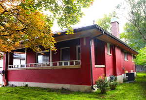 View of side of property featuring brick siding, a chimney, a yard, and covered porch