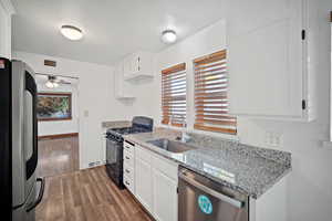 Kitchen featuring appliances with stainless steel finishes, white cabinets, light wood-type flooring, light stone countertops, and ceiling fan