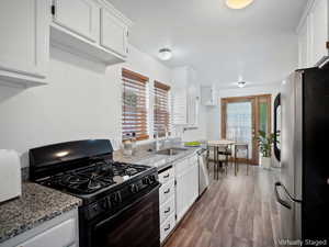 Kitchen featuring stainless steel appliances, white cabinets, light stone counters, and dark wood-style floors