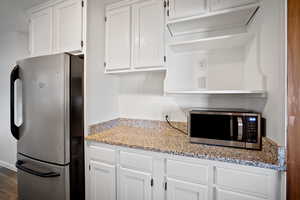 Kitchen with stainless steel appliances, white cabinetry, light stone countertops, and wood finished floors