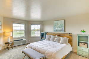 Carpeted bedroom with a textured ceiling and an AC wall unit