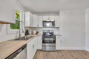 Kitchen featuring appliances with stainless steel finishes, white cabinets, light wood-type flooring, and butcher block counters