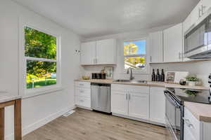 Kitchen featuring appliances with stainless steel finishes, light countertops, white cabinets, and light wood-type flooring