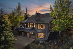 View of front facade with a standing seam roof, stone siding, a metal roof, a chimney, and concrete driveway