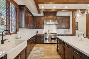 Kitchen featuring dark brown cabinetry, backsplash, decorative light fixtures, double oven range, and light stone counters