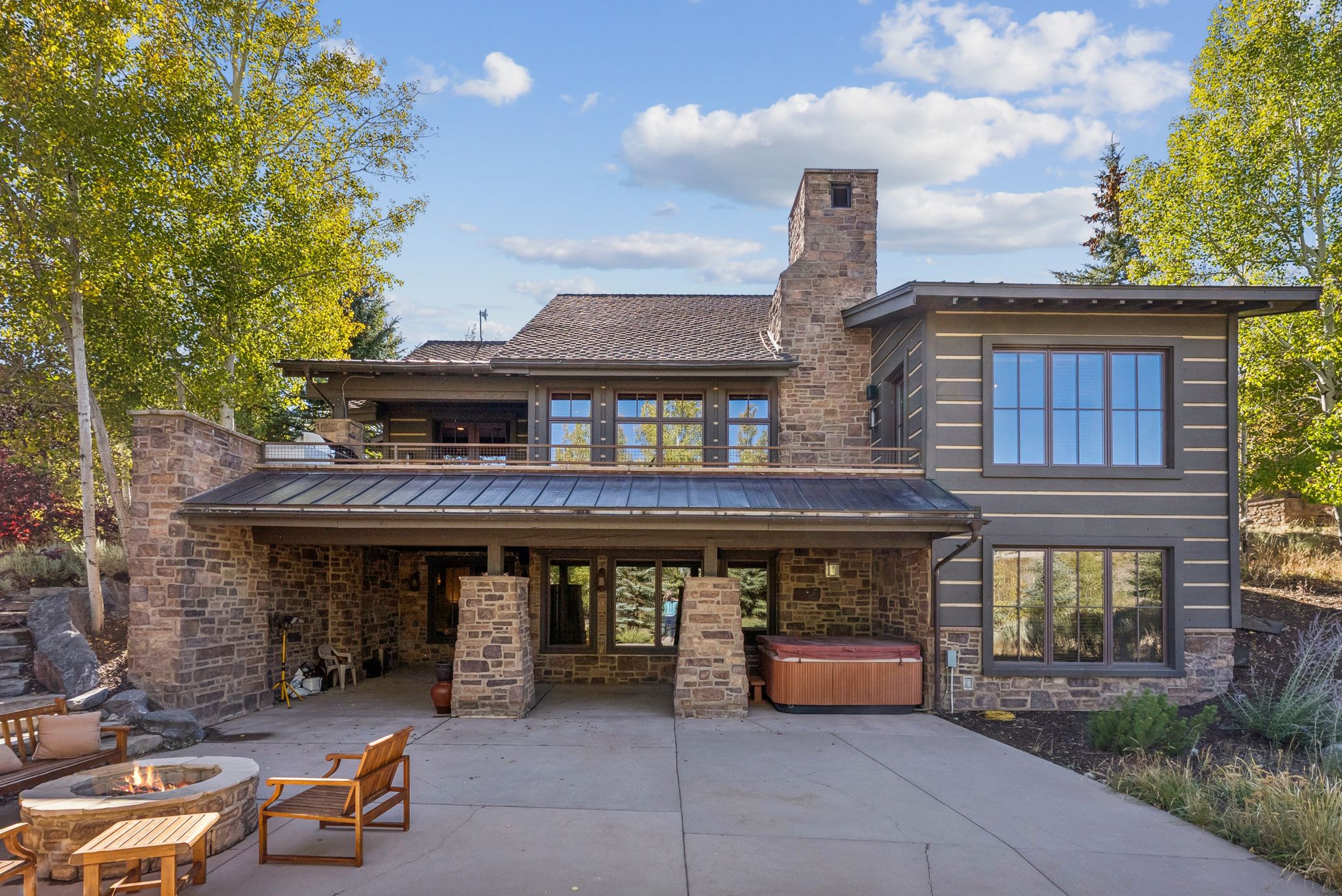 Back of house featuring a fire pit, stone siding, a standing seam roof, a hot tub, and a patio area