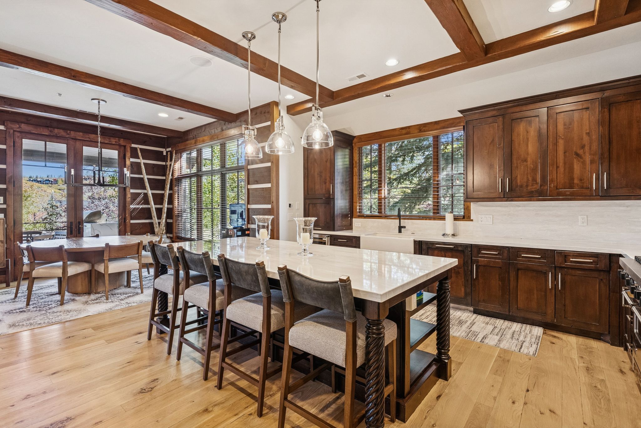 Kitchen featuring beamed ceiling, decorative light fixtures, dark brown cabinetry, light wood-type flooring, and light stone counters