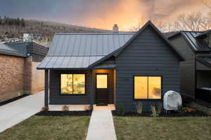 View of front of house with a front yard, a standing seam roof, a chimney, a metal roof, and oil tank
