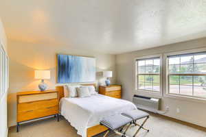Bedroom with carpet, a textured ceiling, and an AC wall unit