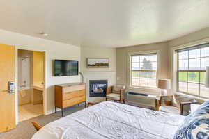 Carpeted bedroom featuring a textured ceiling, a glass covered fireplace, a wall unit AC, and tile patterned flooring